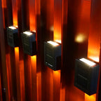 Solar Up & Down Outdoor Wall Lamp in warm white beside a bed